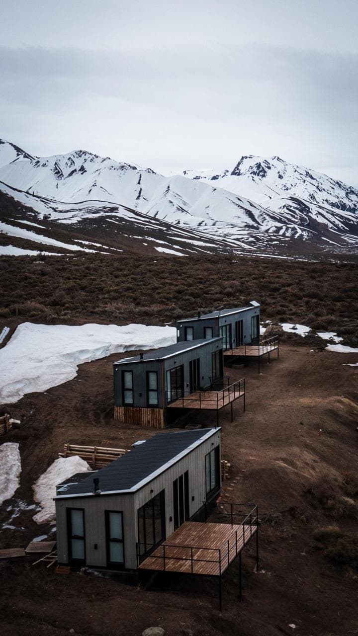 Tres cabañas bajando la ladera con la cordillera completa de fondo