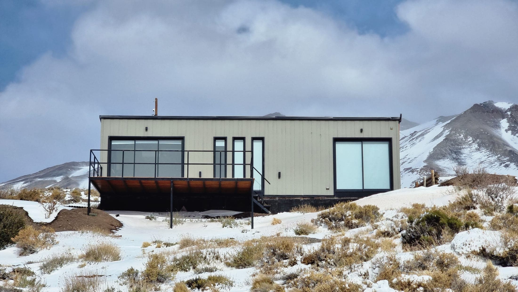 Cabaña 1 completa de frente, cielo dramático y la cordillera de fondo