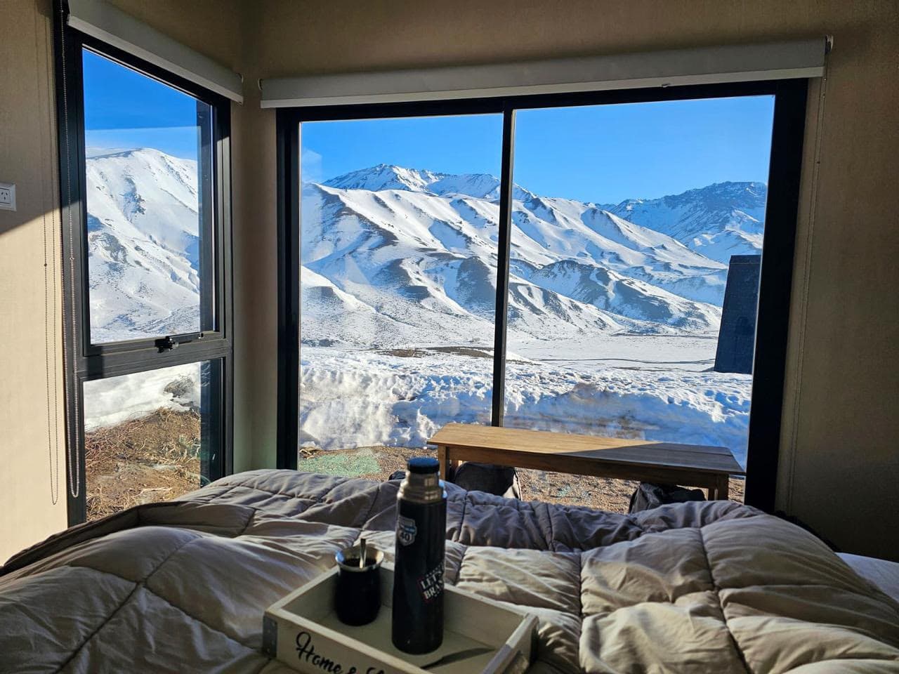 Mate y termo sobre la cama frente al ventanal a la cordillera